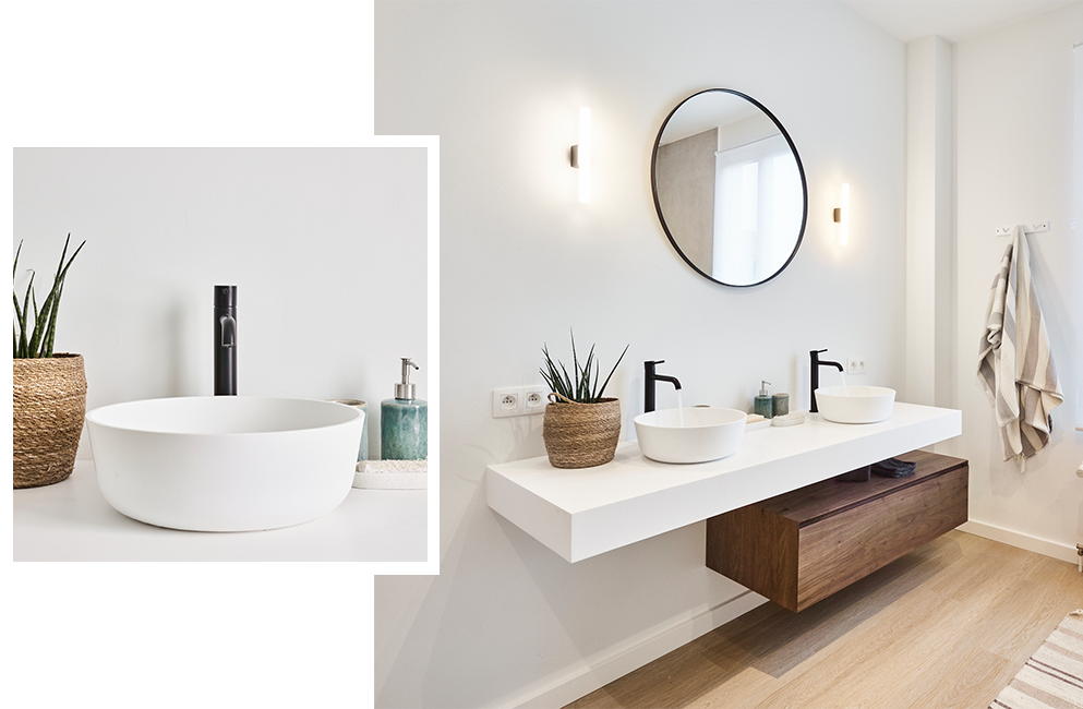 Strakke badkamer met dubbele witte wastafels, zwarte kranen, ronde spiegel en houten meubel.